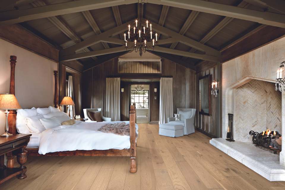 white oak flooring in rustic ski cabin bedroom with vaulted wooden beams, chandelier and stone fireplace